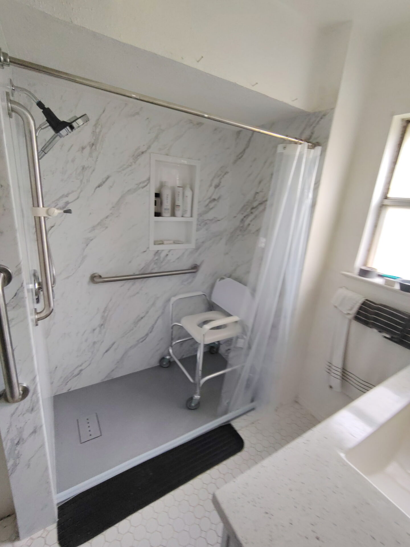AccessAbility shower with a rolling shower chair, grab bars, handheld showerhead, and low entry